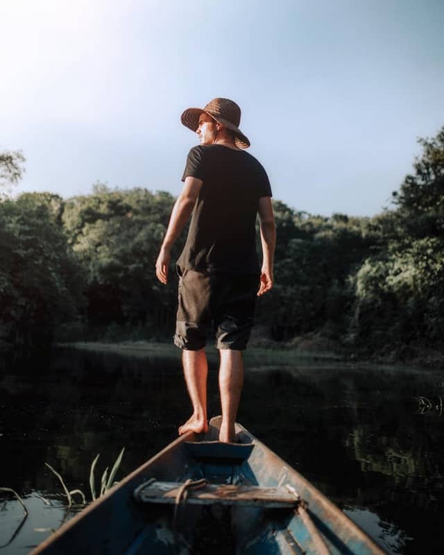 Ein Reisender steht im Morgengrauen am Bug eines Holzkanus auf ruhigem Schwarzwasser bei einer Amazonas-Tour