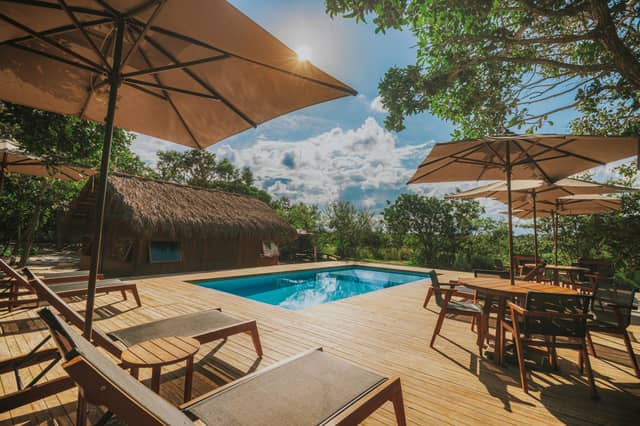 Zonnig houten pooldek met ligstoelen, parasols en een rieten ecolodge omringd door tropisch woud tijdens een luxe reis door Brazilië