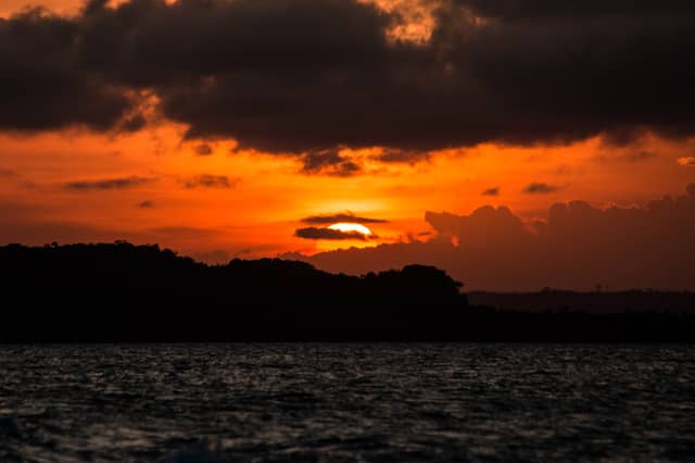 Glutrot-orangefarbener Sonnenuntergang über der Silhouette der Atlantikwald-Küste von Itacaré, gespiegelt auf dunklem, bewegtem Wasser