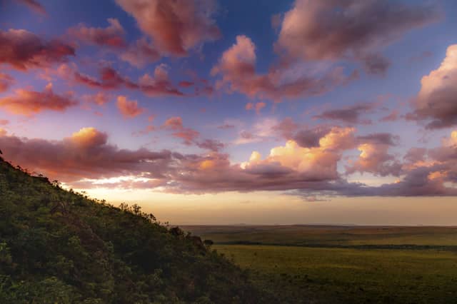 Vista panorâmica do pôr do sol sobre o Cerrado plano do Jalapão, com nuvens cor-de-rosa e douradas cobrindo um vasto céu sobre uma encosta arborizada no Tocantins, Brasil