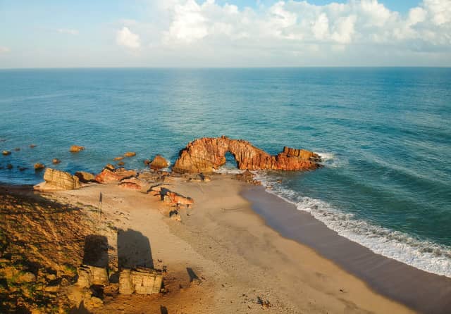 A natural red sandstone arch rising from the sea on a secluded beach, a dramatic coastal landmark discovered on brazil private tours