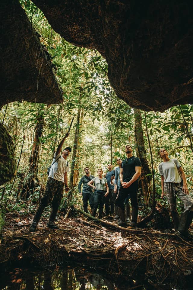 A small group and their guide on an Amazon jungle tour, pausing beneath a giant rock overhang in the rainforest
