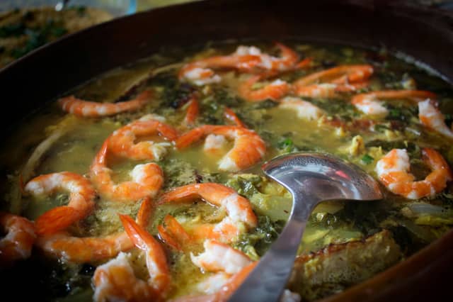 Clay pot of Amazonian shrimp and jambu stew in golden tucupi broth with a serving ladle