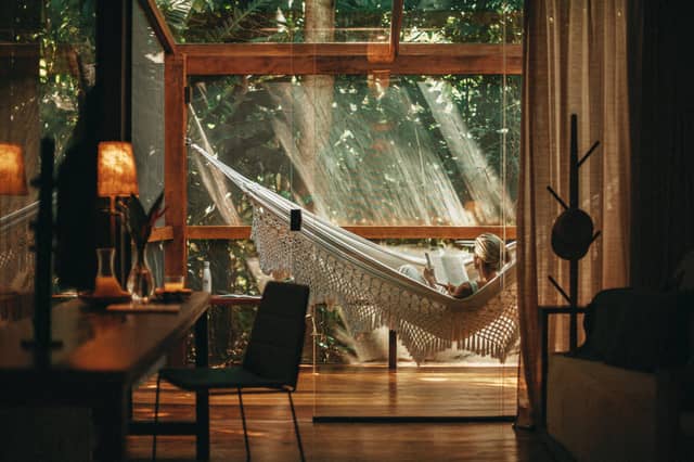 A woman reading a book in a macramé hammock on the sunlit terrace of a brazil luxury tours jungle lodge, surrounded by lush rainforest and warm timber interiors