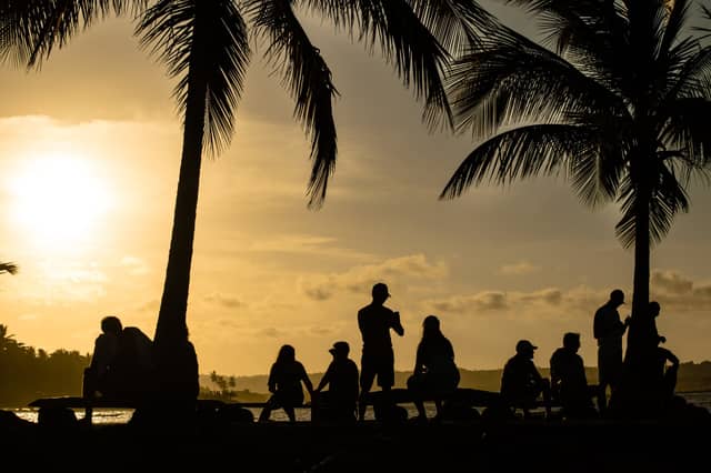 Silhouette di un gruppo di viaggiatori riuniti sotto alte palme mentre osservano un tramonto dorato sull'acqua durante un tour a Itacaré, Bahia, Brasile