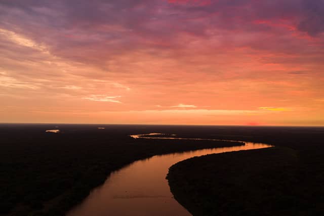 Aerial view of a winding river snaking through the vast Pantanal wetlands of Brazil at sunset, with the sky blazing in shades of orange, red, and violet