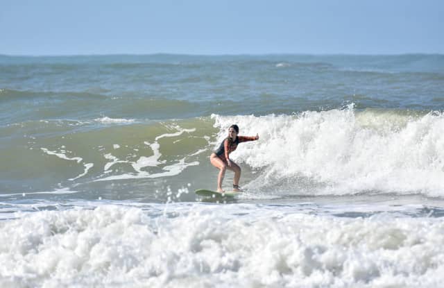 A woman crouches low on a surfboard while taking surf lessons in Itacaré, riding a foaming wave under a clear blue sky