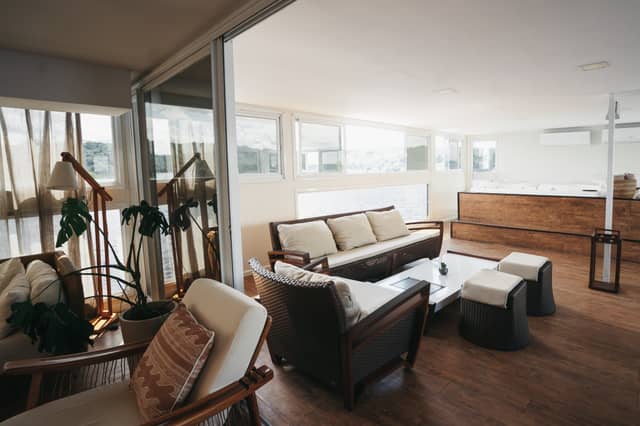 Bright, airy lounge on the untamed amazon cruise with rattan sofas, warm timber floors, a monstera plant, and panoramic windows overlooking the river