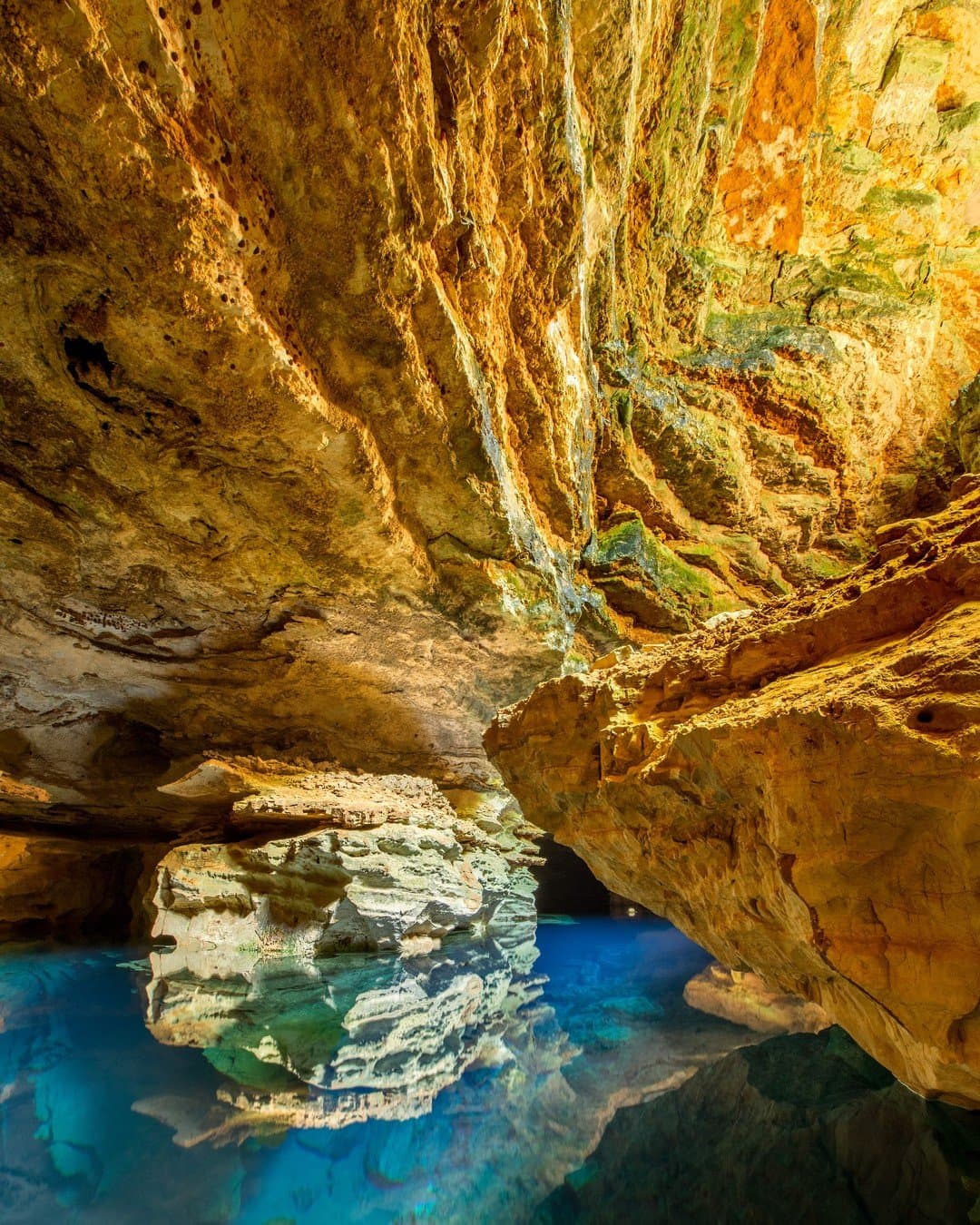 Turquoise underground pool reflecting golden limestone cave walls on a Chapada Diamantina trip, with sculpted rock formations rising from mirror-still water