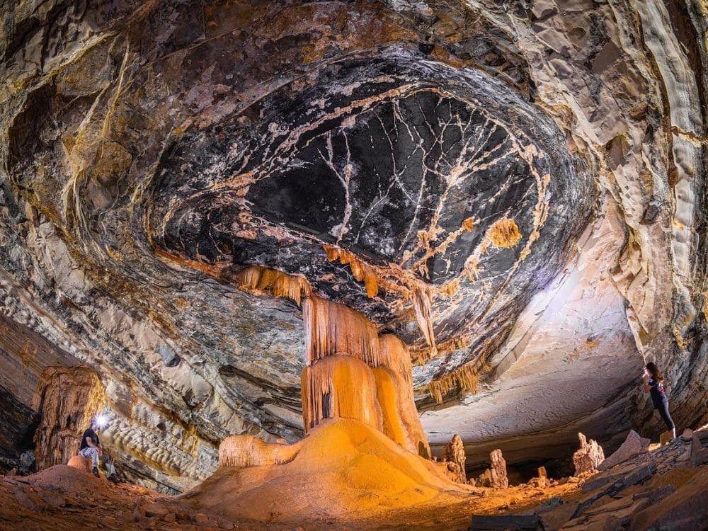 Interno di una grotta con formazioni geologiche imponenti, stalattiti e stalagmiti sotto una luce artificiale calda, nella Chapada Diamantina.