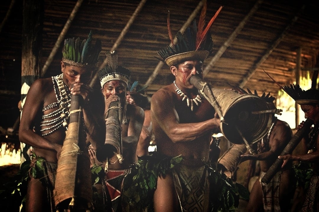 Indigeni dell'Amazzonia suonano strumenti a fiato tradizionali durante una presentazione culturale.