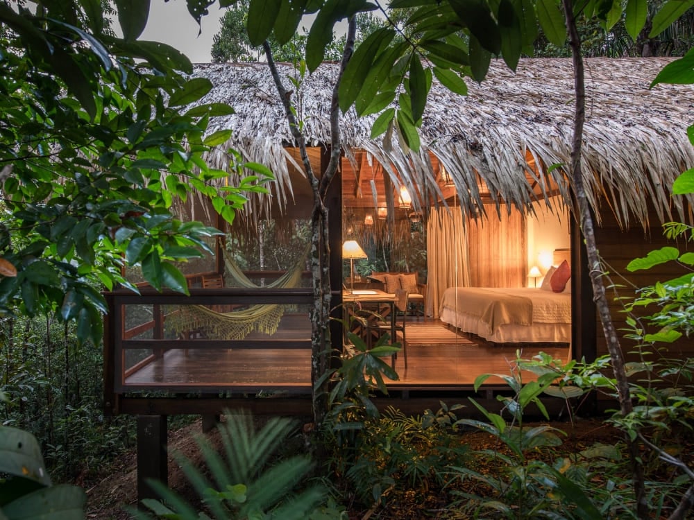 A refined bungalow with a thatched roof and a hammock on the balcony at Anavilhanas Jungle Lodge in Brazil.