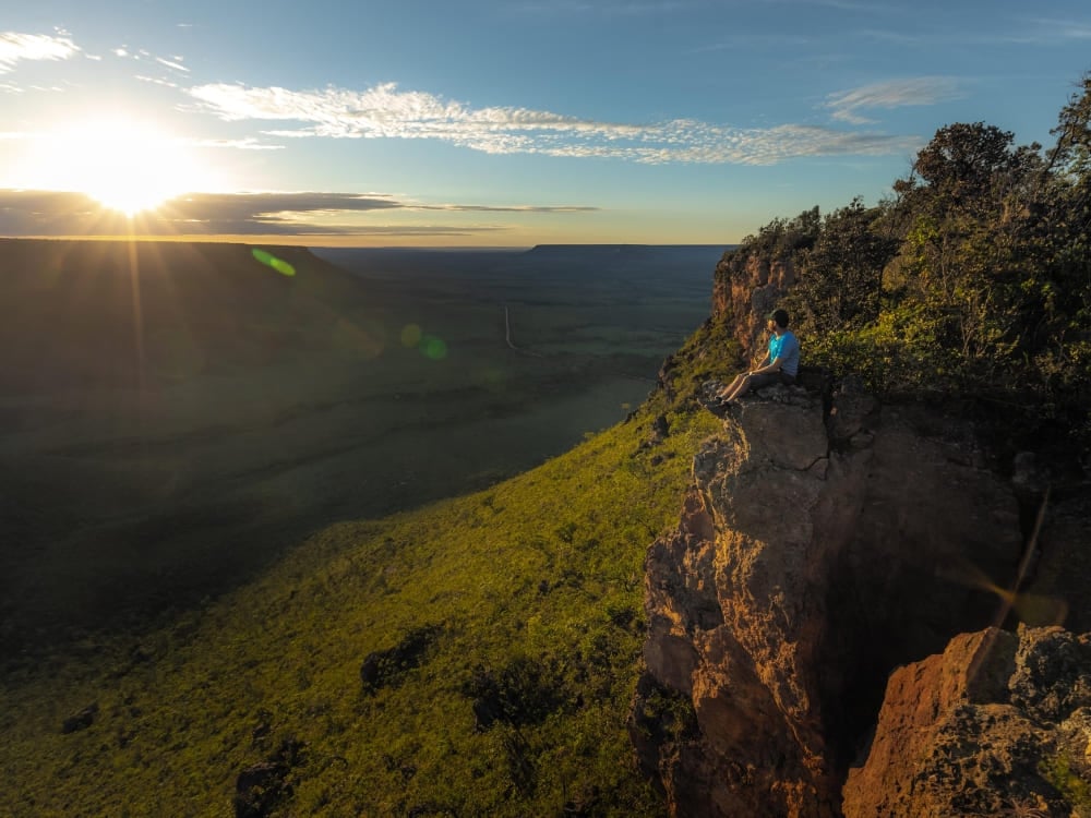 Un viaggiatore seduto sul bordo di una falesia guarda il tramonto sull'ampia savana del Parco Statale del Jalapão.