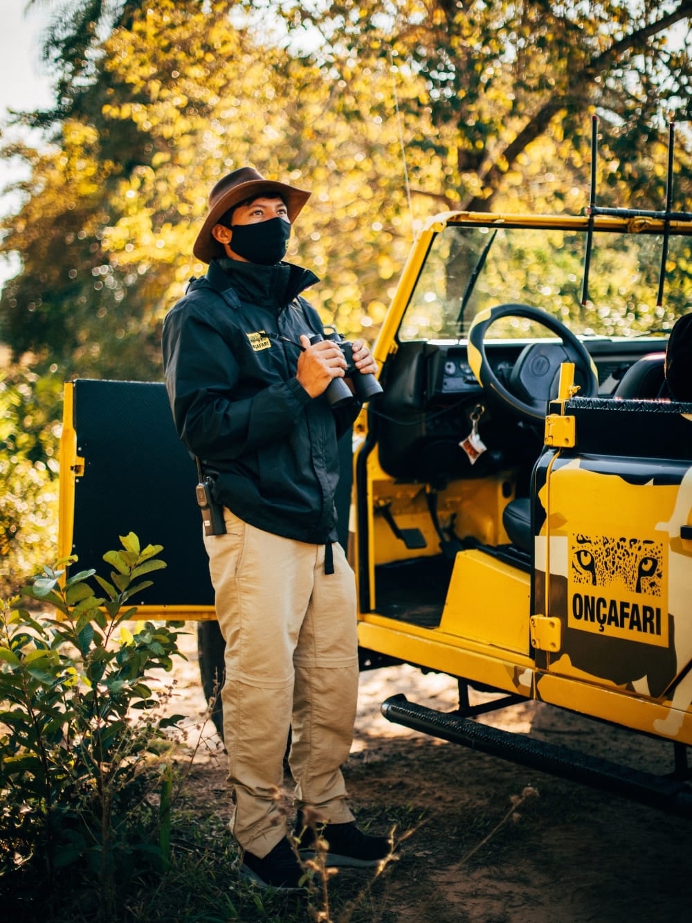 An ecotourism guide holding binoculars standing next to an Onçafari project vehicle.