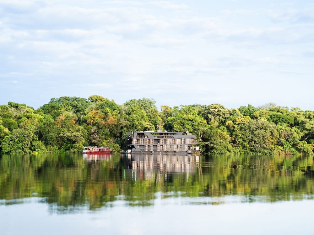 Una barca da crociera fluviale a più ponti in Amazzonia galleggia su acque calme che riflettono la fitta vegetazione verde della foresta.