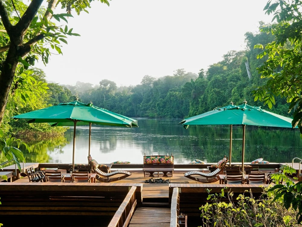Wooden deck with green umbrellas and lounge chairs overlooking a serene Amazon river.