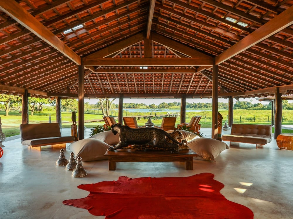Open-air living room featuring a red cowhide rug and a carved wooden jaguar at Caiman ecolodge.