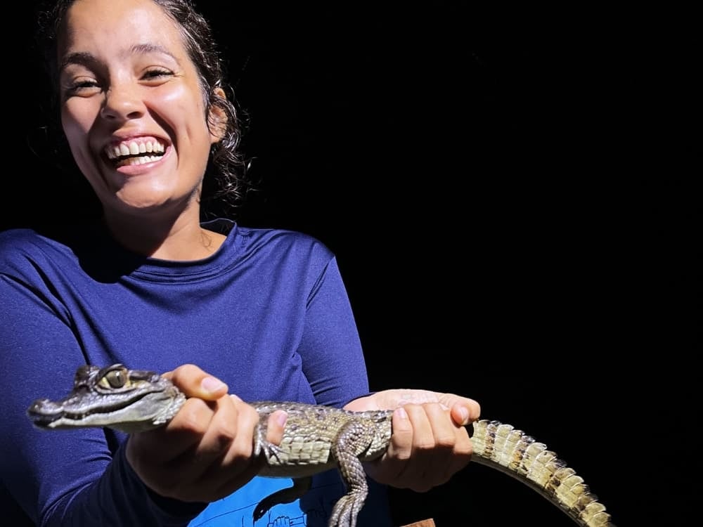 Mariana sorride entusiasta mentre tiene in mano in sicurezza un piccolo caimano durante un'escursione notturna in Amazzonia.