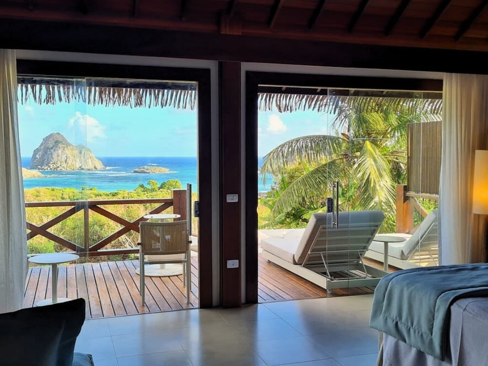 Open balcony doors revealing a lounge chair and stunning ocean views in Fernando de Noronha.