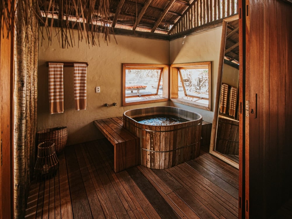 Wooden soaking tub set beside large windows inside a rustic suite at Pousada Trijuncao.