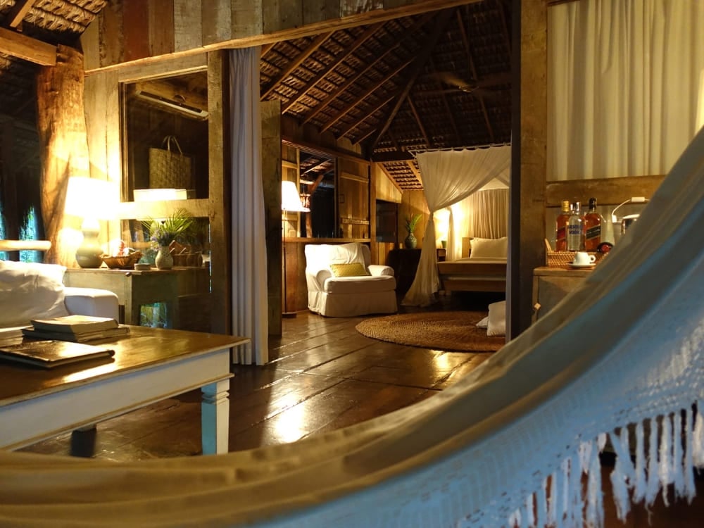 View from a hammock looking into a warmly lit rustic suite with wooden floors at UXUA.