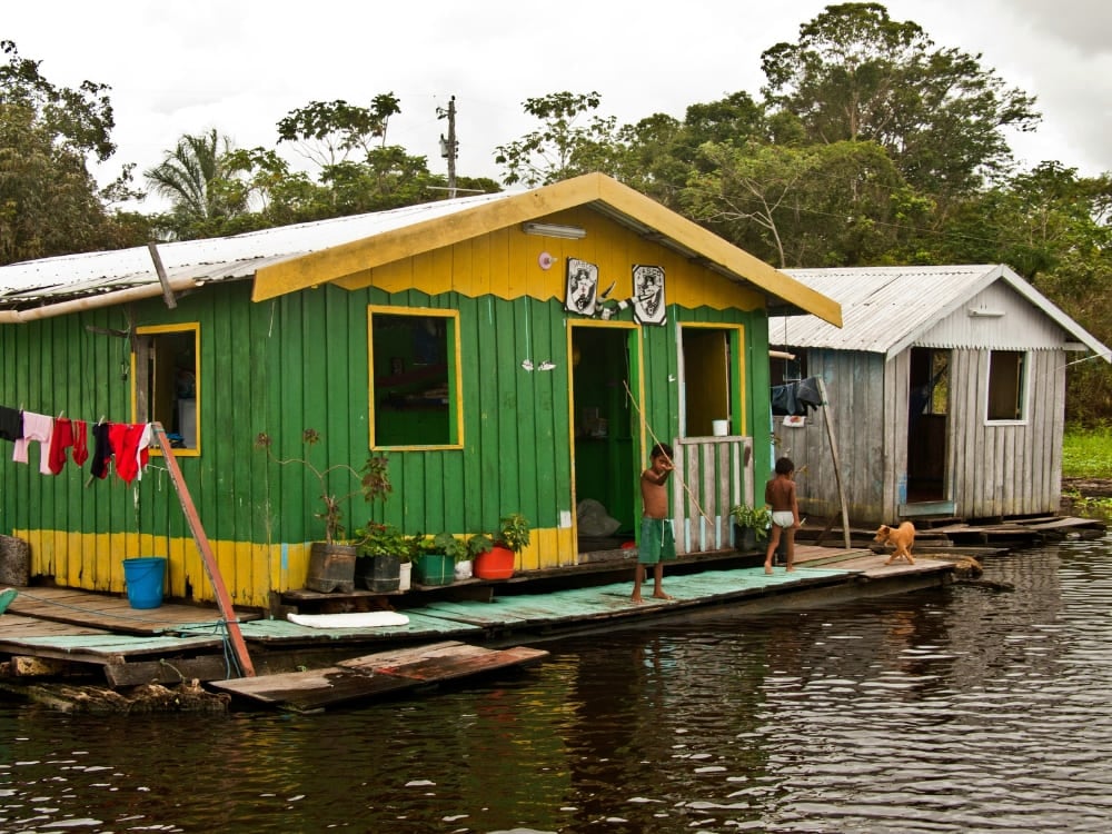 Children standing outside a vibrant green and yellow floating house on the waters of the Amazon River.