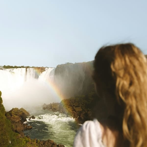 A visitor looking out over the Iguaçu Falls with a rainbow in the spray, Brazil.