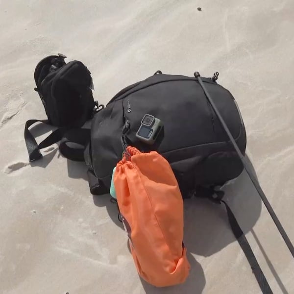 Backpacks, an action camera and an orange dry bag resting on the sand during a break on the trek