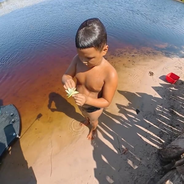 Local child holding a flower at the edge of a lagoon