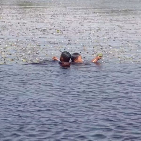 Two children swimming in a lagoon in Lençóis Maranhenses, one of them holding a leaf above the water