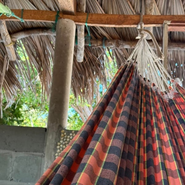 Striped hammock hanging under a thatched roof, the typical bed on the Lençóis Maranhenses trek