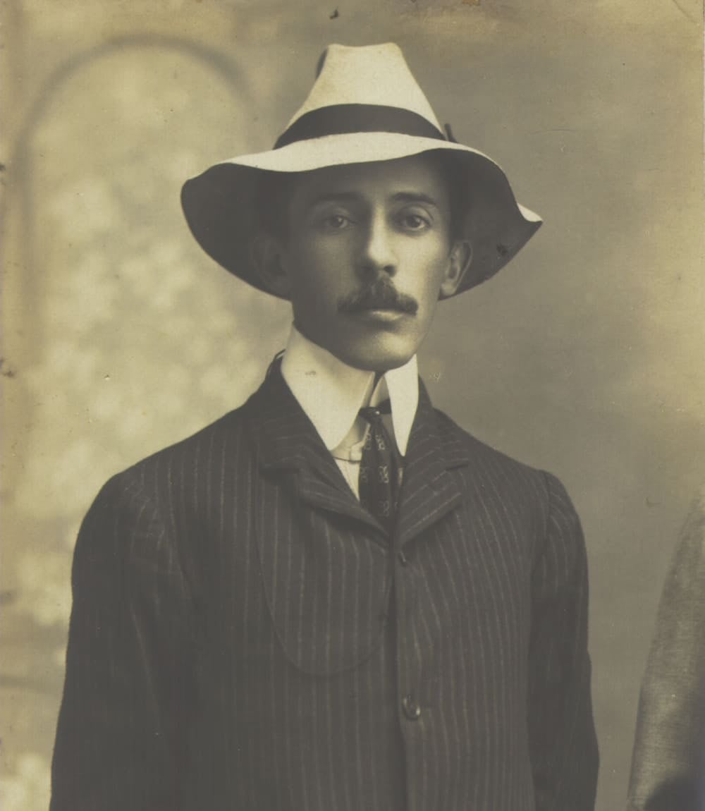 Retrato de estudio en sepia del pionero brasileño de la aviación Santos Dumont, con sombrero blanco y traje de raya diplomática