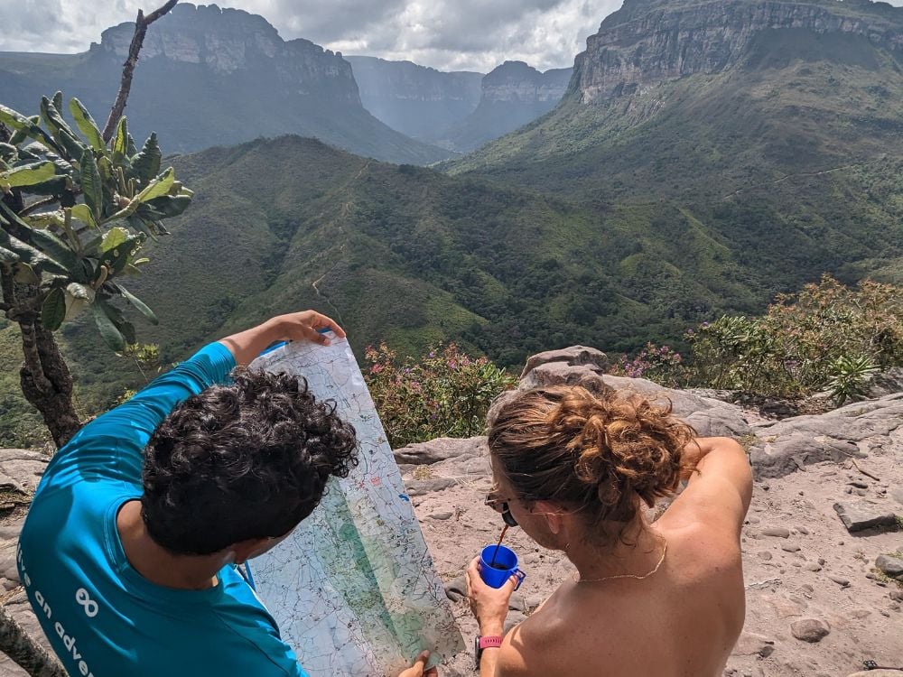 Ein einheimischer Guide in einem blauen Hemd und ein Wanderer betrachten gemeinsam eine Wanderkarte, während sie sich an einem Aussichtspunkt im Tal ausruhen. Ein einheimischer Guide in einem blauen Hemd und ein Wanderer betrachten gemeinsam eine Wanderkarte, während sie sich an einem Aussichtspunkt im Tal ausruhen.