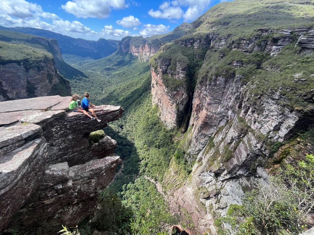 Zwei Personen sitzen am Rand einer dramatischen, 300 Meter hohen Canyon-Klippe am Cachoeirão und bewundern die steilen Felswände. Zwei Personen sitzen am Rand einer dramatischen, 300 Meter hohen Canyon-Klippe am Cachoeirão und bewundern die steilen Felswände.