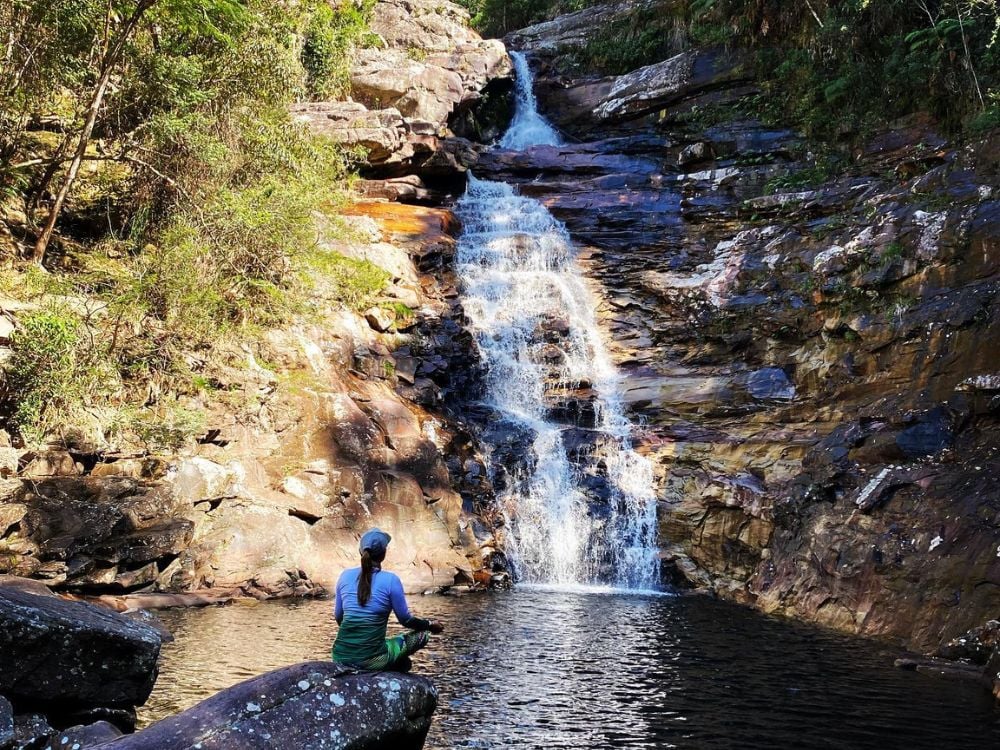Eine Frau sitzt friedlich auf einem Felsen neben dem natürlichen Becken am Fuße des 30 Meter hohen Funis-Wasserfalls. Eine Frau sitzt friedlich auf einem Felsen neben dem natürlichen Becken am Fuße des 30 Meter hohen Funis-Wasserfalls.