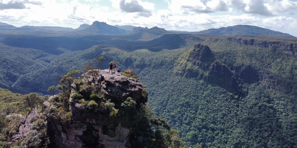 Wanderer stehen auf einem felsigen Gipfel am Morro do Castelo und blicken über einen riesigen, bewaldeten Canyon in der Chapada Diamantina. Wanderer stehen auf einem felsigen Gipfel am Morro do Castelo und blicken über einen riesigen, bewaldeten Canyon in der Chapada Diamantina.