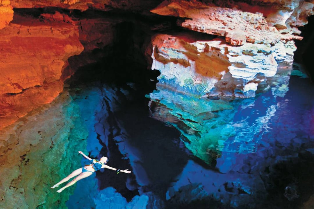 Una donna galleggia sulla schiena nell'acqua azzurra e cristallina di una piscina naturale sotterranea, circondata da pareti di roccia. Una donna galleggia sulla schiena nell'acqua azzurra e cristallina di una piscina naturale sotterranea, circondata da pareti di roccia.