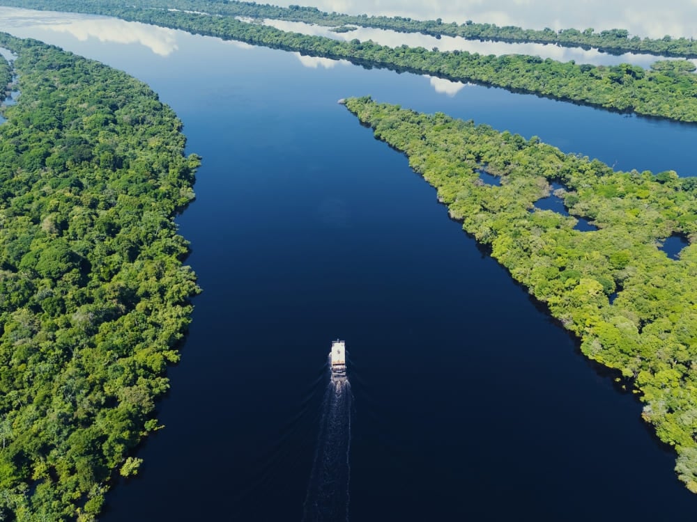 Un battello a più ponti naviga lungo un ampio fiume scuro e calmo, circondato da fitte isole di foresta verde che riflettono il cielo. Un battello a più ponti naviga lungo un ampio fiume scuro e calmo, circondato da fitte isole di foresta verde che riflettono il cielo.