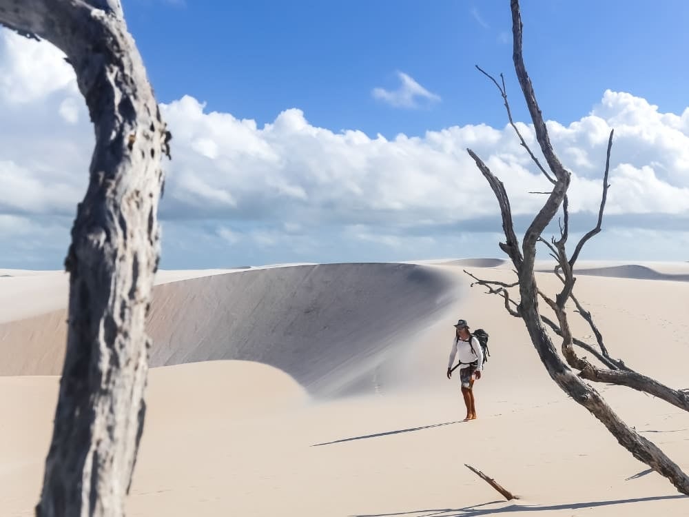 Ein Wanderer geht über die weiten weißen Sanddünen des Nationalparks Lençóis Maranhenses, eingerahmt von trockenen Ästen unter einem blauen Himmel. Ein Wanderer geht über die weiten weißen Sanddünen des Nationalparks Lençóis Maranhenses, eingerahmt von trockenen Ästen unter einem blauen Himmel.