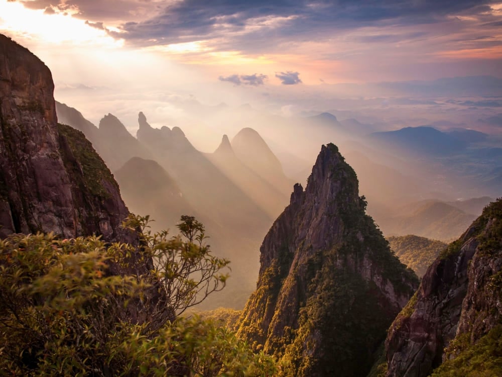 Dramatische, zerklüftete Berggipfel ragen bei Sonnenaufgang durch dichten Nebel im Nationalpark Serra dos Órgãos auf und heben die Felsformation Dedo de Deus hervor. Dramatische, zerklüftete Berggipfel ragen bei Sonnenaufgang durch dichten Nebel im Nationalpark Serra dos Órgãos auf und heben die Felsformation Dedo de Deus hervor.