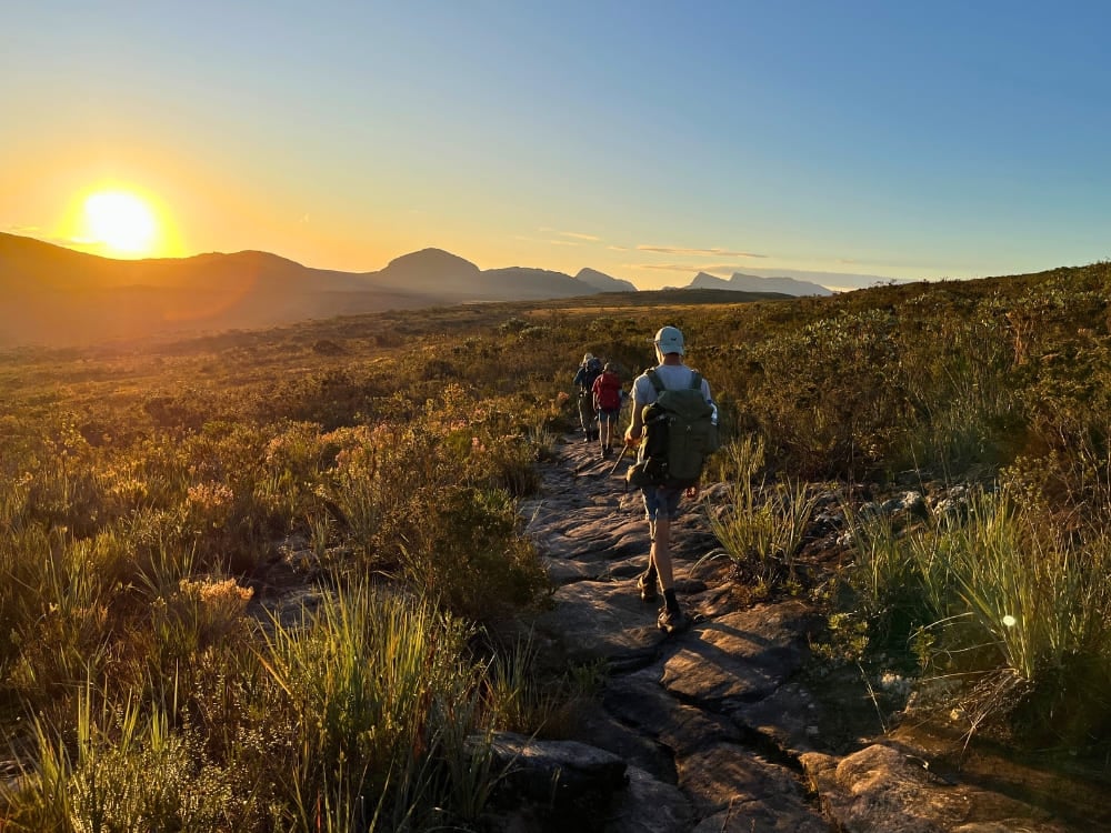 Wanderer laufen auf einem felsigen Pfad in Richtung weit entfernter Berge während eines goldenen Sonnenuntergangs im Vale do Pati, Nationalpark Chapada Diamantina. Wanderer laufen auf einem felsigen Pfad in Richtung weit entfernter Berge während eines goldenen Sonnenuntergangs im Vale do Pati, Nationalpark Chapada Diamantina.