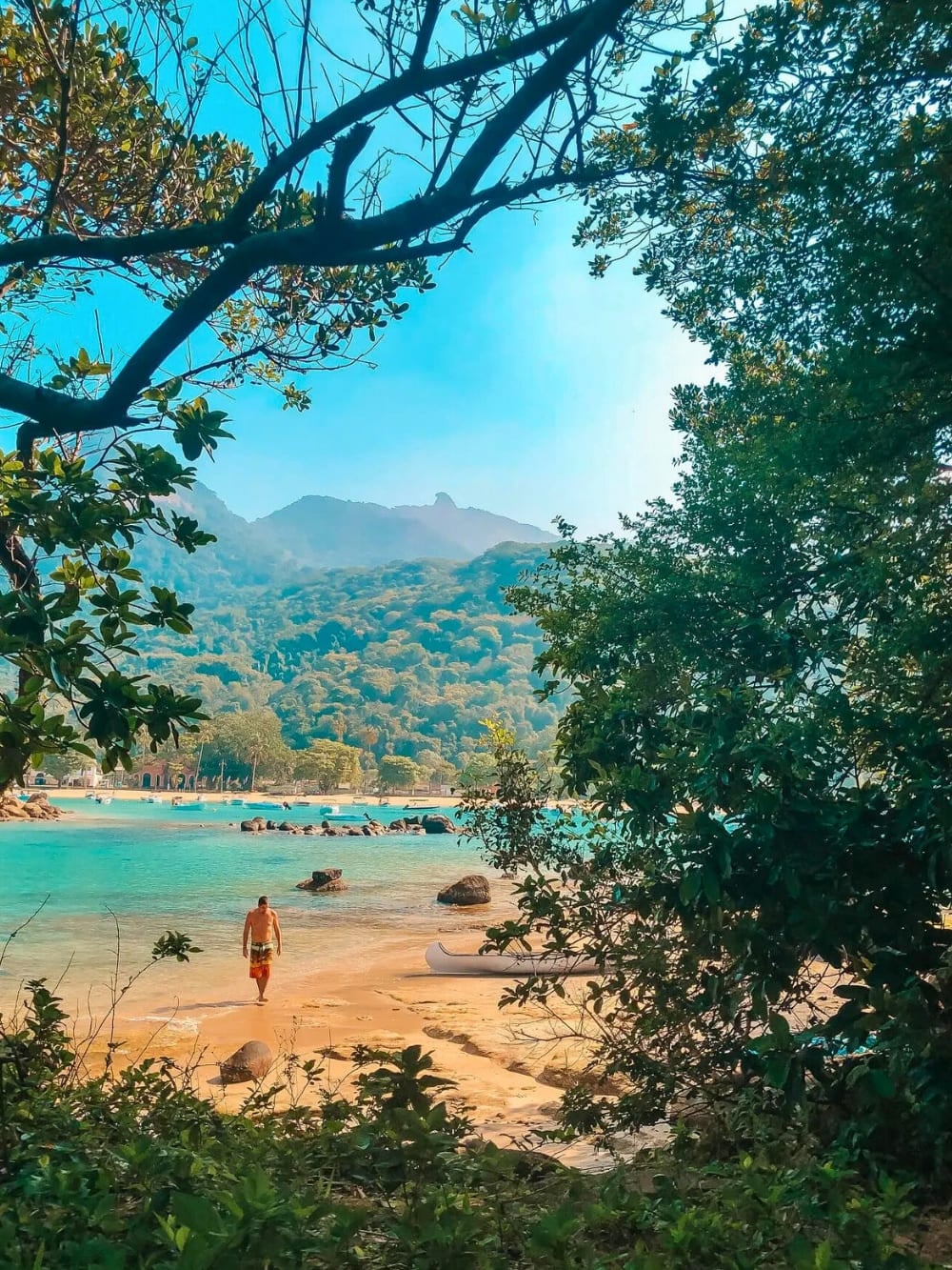 Eine Person geht am unberührten weißen Sand und klaren blauen Wasser des Lopes Mendes Strandes auf der Ilha Grande entlang, umgeben von tropischem Wald und Bergen. Eine Person geht am unberührten weißen Sand und klaren blauen Wasser des Lopes Mendes Strandes auf der Ilha Grande entlang, umgeben von tropischem Wald und Bergen.
