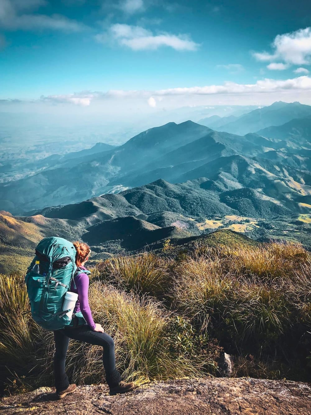 Ein Wanderer mit einem großen grünen Rucksack steht auf einem grasbewachsenen Bergrücken und blickt auf die weitläufige, bergige Landschaft der Serra Fina. Ein Wanderer mit einem großen grünen Rucksack steht auf einem grasbewachsenen Bergrücken und blickt auf die weitläufige, bergige Landschaft der Serra Fina.