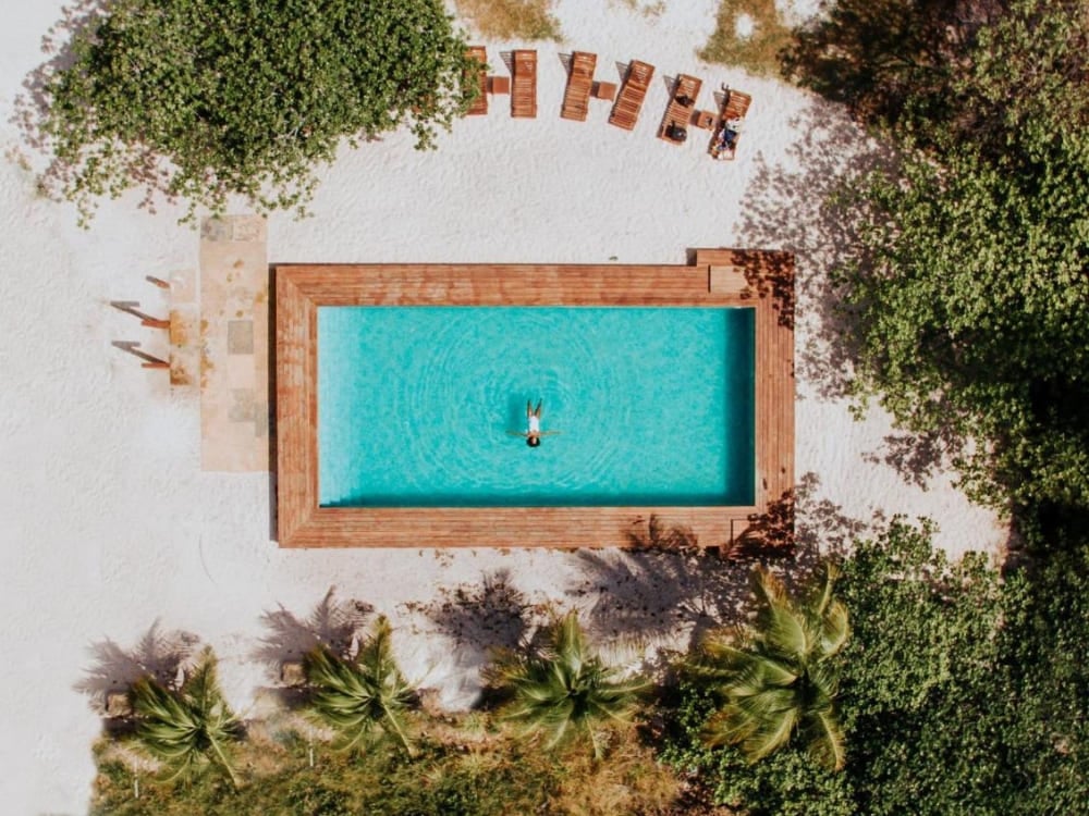 Scatto aereo verticale di una piscina rettangolare color turchese, con un deck di legno liscio e i lettini, nel lussuoso La Ferme De Georges. Scatto aereo verticale di una piscina rettangolare color turchese, con un deck di legno liscio e i lettini, nel lussuoso La Ferme De Georges.
