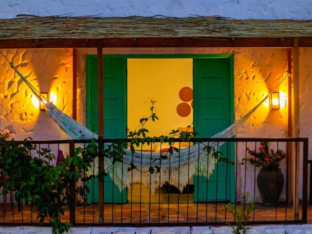 Balconcino raccolto, illuminato di notte, con un'amaca tesa davanti alla porta a due battenti verde di uno chalet della Quintal das Areias. Balconcino raccolto, illuminato di notte, con un'amaca tesa davanti alla porta a due battenti verde di uno chalet della Quintal das Areias.