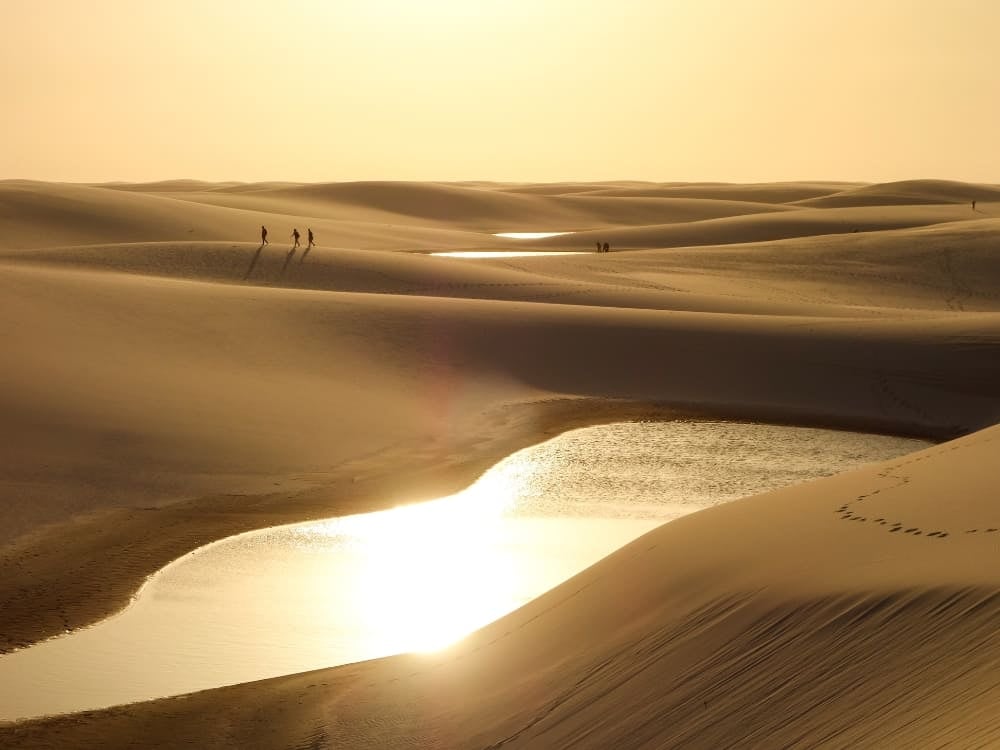 Viaggiatori attraversano la vasta distesa di dune dei Lençóis Maranhenses durante un tramonto luminoso. Viaggiatori attraversano la vasta distesa di dune dei Lençóis Maranhenses durante un tramonto luminoso.