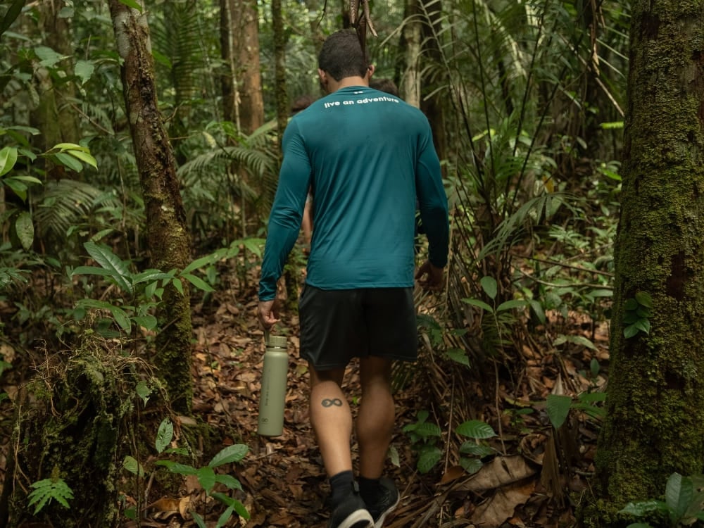 Un viaggiatore con una borraccia riutilizzabile cammina lungo un sentiero verde e rigoglioso della foresta amazzonica. Un viaggiatore con una borraccia riutilizzabile cammina lungo un sentiero verde e rigoglioso della foresta amazzonica.
