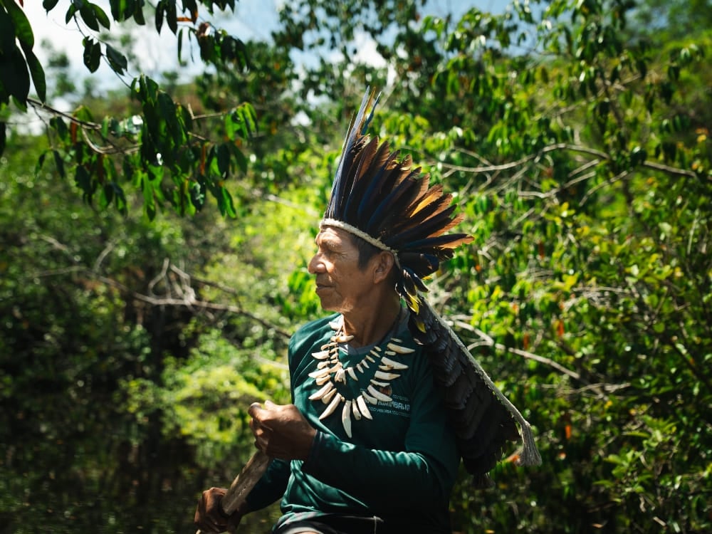Un uomo indigeno con un copricapo tradizionale di piume cammina nella giungla amazzonica verde e rigogliosa. Un uomo indigeno con un copricapo tradizionale di piume cammina nella giungla amazzonica verde e rigogliosa.