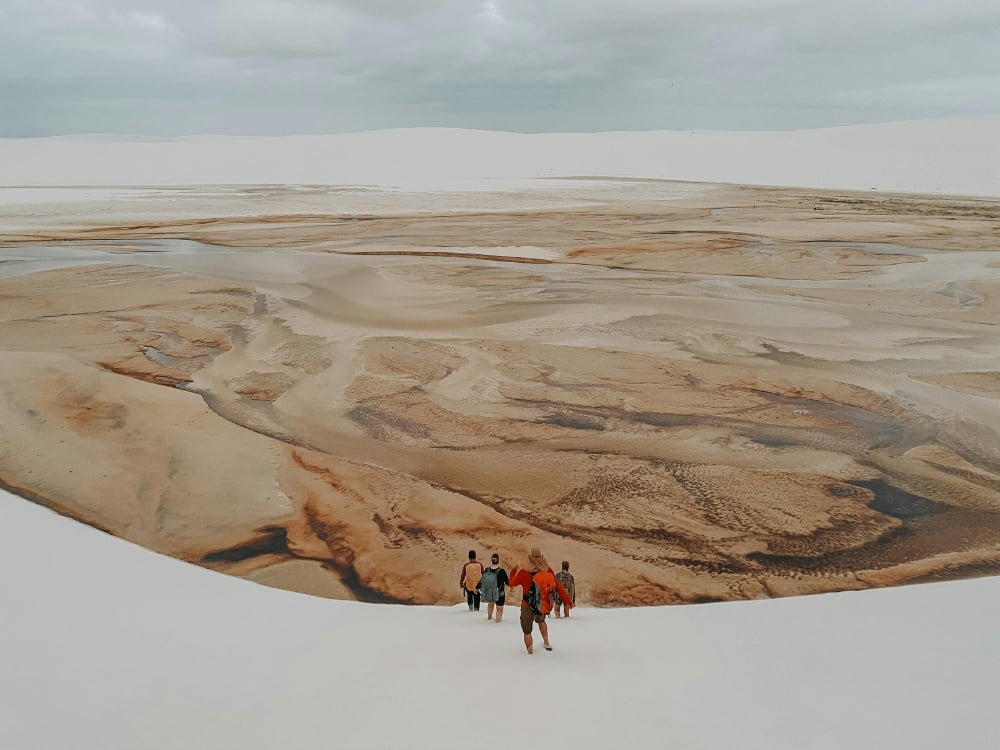 Un grupo de turistas camina por el lecho seco y marrón de una laguna rodeada de grandes dunas de arena blanca durante la temporada seca. Un grupo de turistas camina por el lecho seco y marrón de una laguna rodeada de grandes dunas de arena blanca durante la temporada seca.