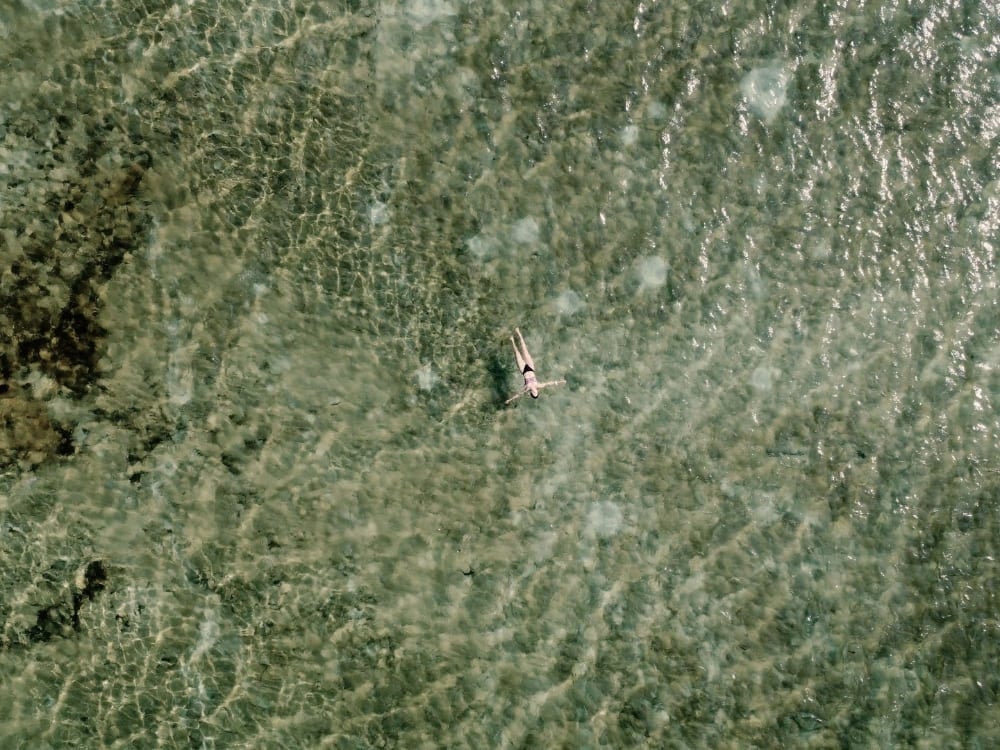 Vista cenital de una persona nadando en una laguna de agua de lluvia cristalina en los Lençóis Maranhenses, con el fondo de arena a la vista. Vista cenital de una persona nadando en una laguna de agua de lluvia cristalina en los Lençóis Maranhenses, con el fondo de arena a la vista.